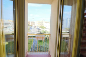 A balcony with a yellow railing, a view of a parking lot, and buildings in the background.