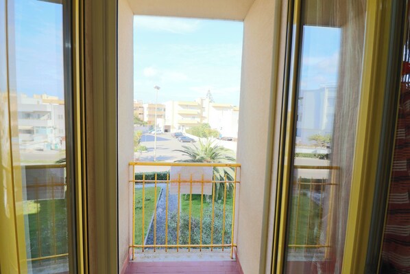 A balcony with a yellow railing, a view of a parking lot, and buildings in the background.