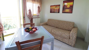 A dining area with a glass table, chairs, a bowl of fruit, a sofa, and two wall-mounted paintings. - Casa Lucia Sea Breeze, Comfort and Relaxation by the Otranto Lighthouse (Otranto)