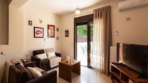 Een woonkamer met een bank, salontafel en tv-meubel. Er hangen ingelijste foto's aan de muur en een schuifpui leidt naar een buitenruimte.
