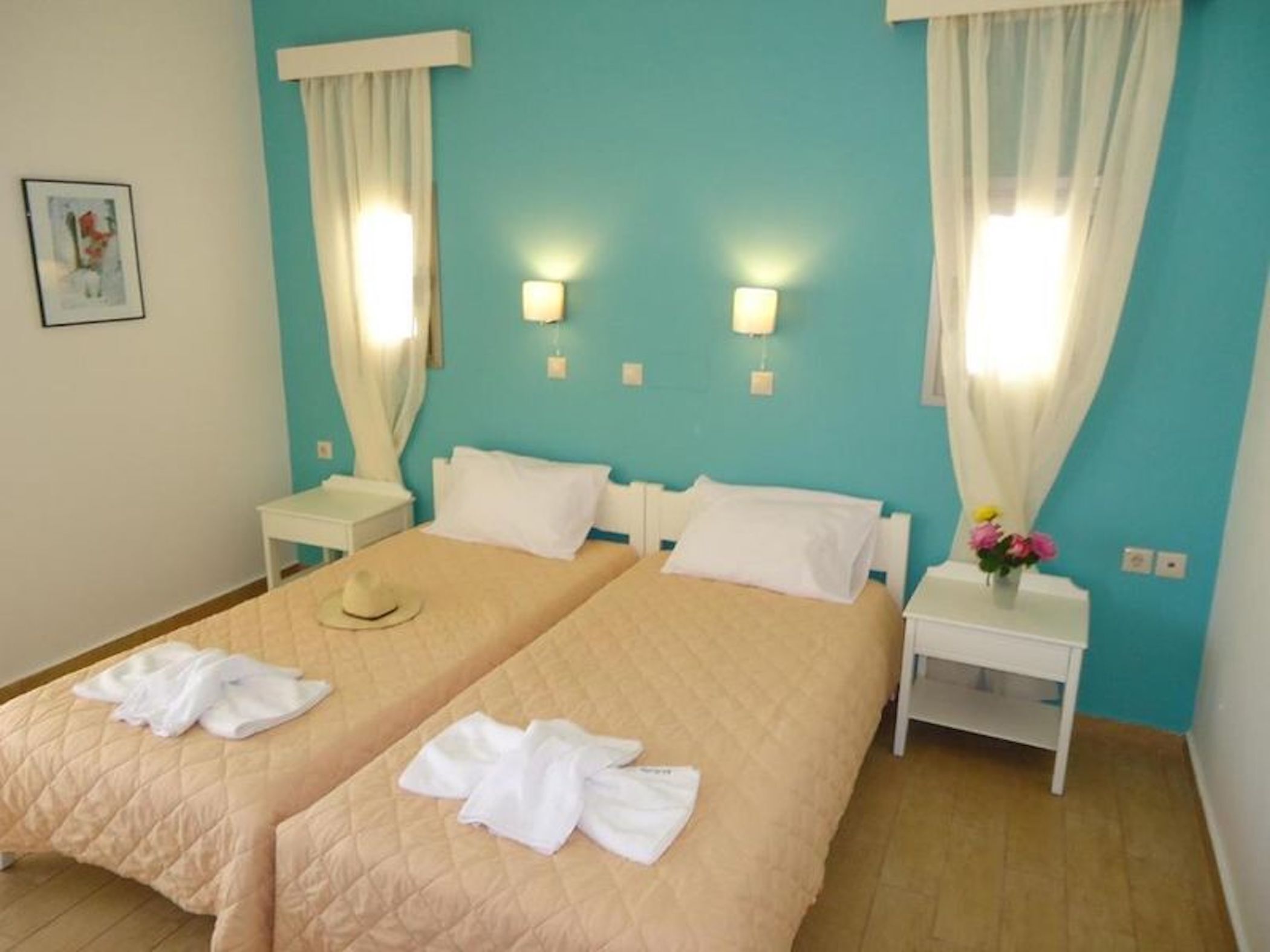 A hotel room with two beds, white linens, a small table, and a nightstand.