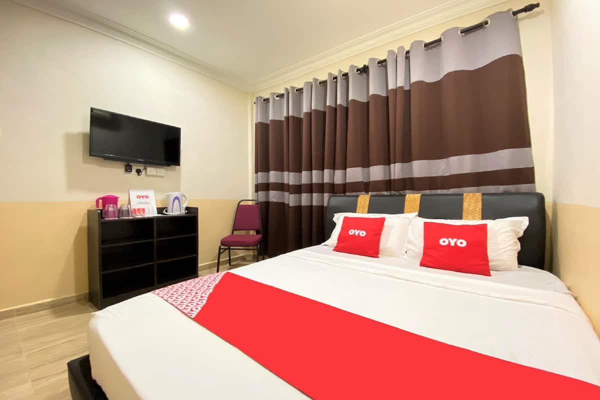 Habitació d'hotel amb llit, televisió penjada a la paret, escriptori amb cadira i finestra amb cortines.
