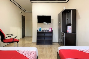 A hotel room with two beds, a TV mounted on the wall, a cabinet with a mirror, and a shelf with toiletries.
