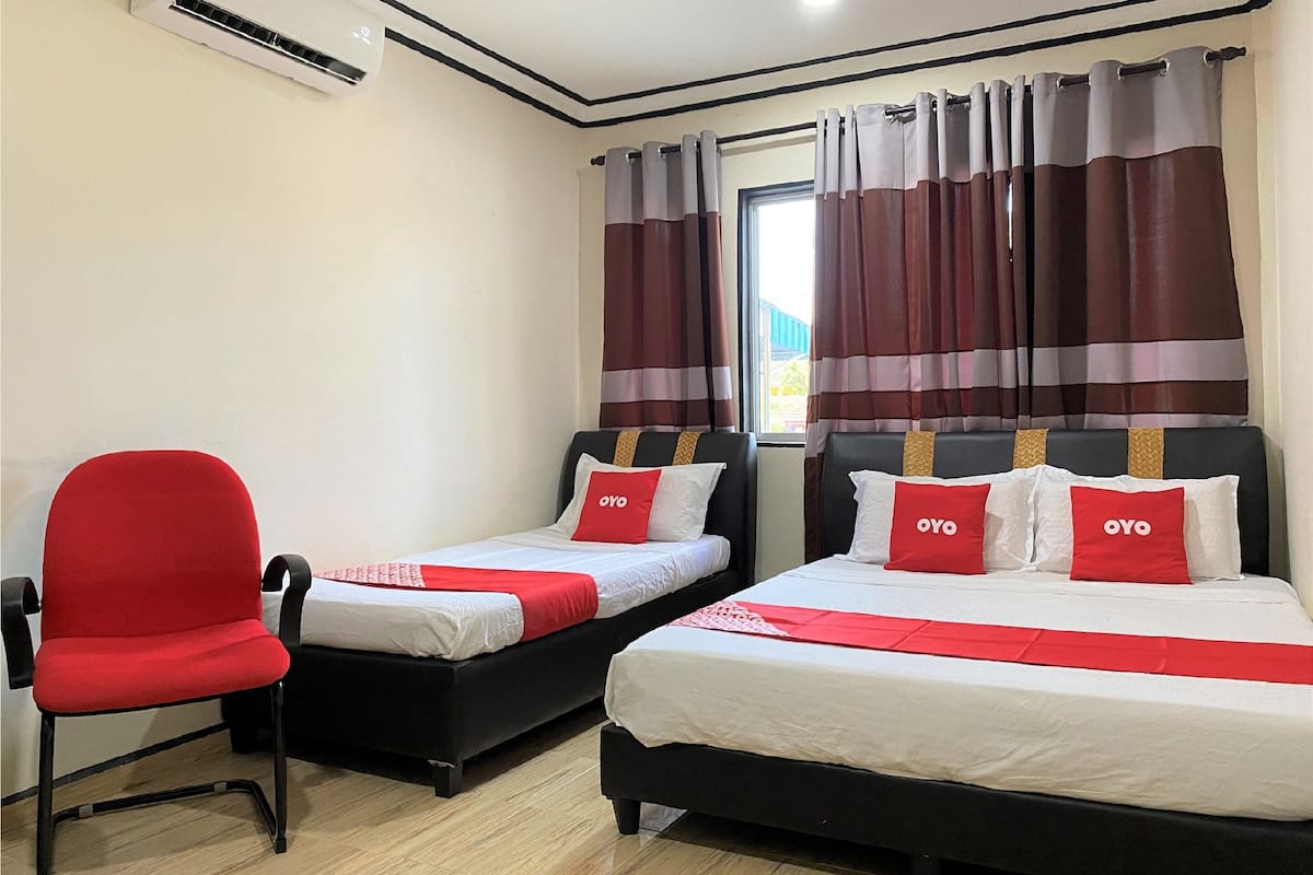 Una habitació d'hotel amb dos llits, una cadira vermella i una finestra amb cortines a ratlles.
