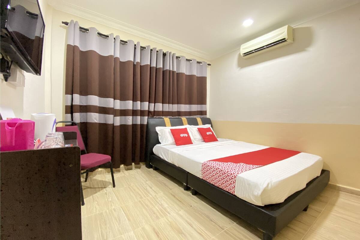 Habitació d'hotel amb un llit, escriptori, cadira, mirall, cortines i aparell d'aire condicionat.