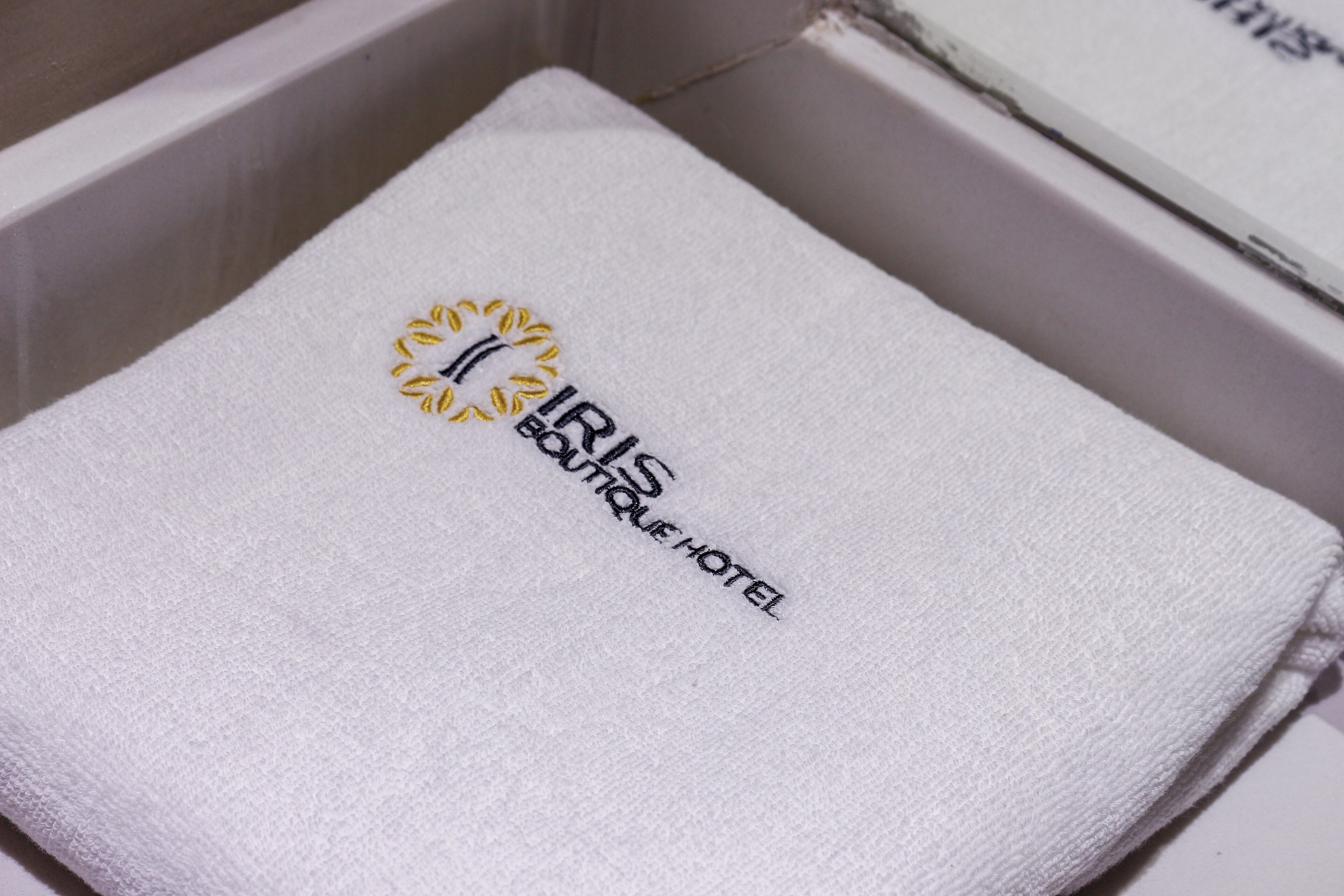 Asciugamano bianco con ricami di testo e logo, presentato in una scatola bianca.