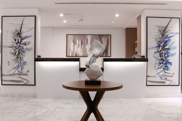 Un área de recepción con diseño moderno, que presenta arte abstracto en las paredes, una escultura central sobre una mesa redonda y un elegante mostrador de recepción.