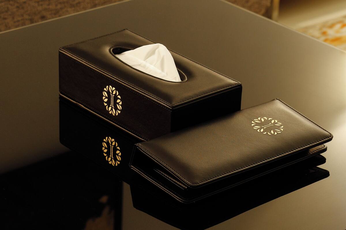 Eine schwarze Lederbox mit Taschentuch und passendem Portemonnaie auf einer spiegelnden Oberfläche.