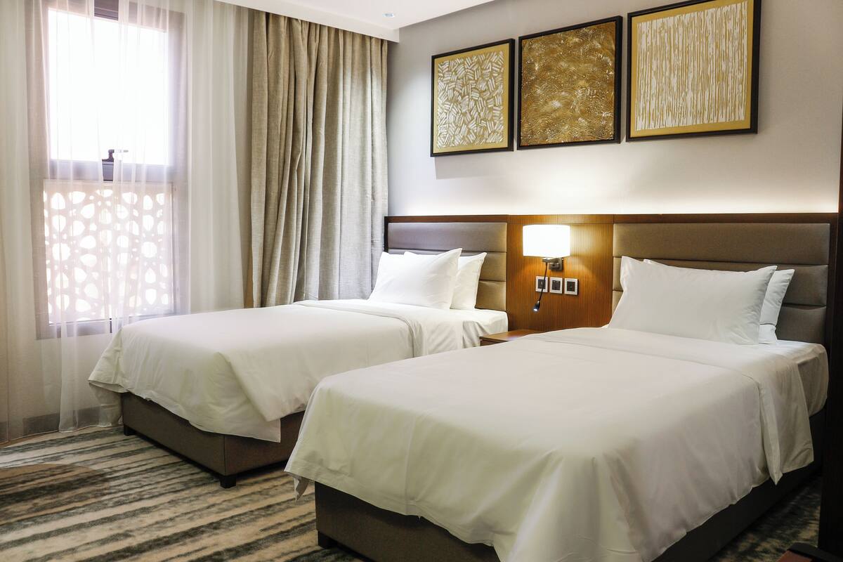 Ein Hotelzimmer mit zwei Betten, einem großen Fenster mit Vorhängen und drei gerahmten Kunstwerken an der Wand.