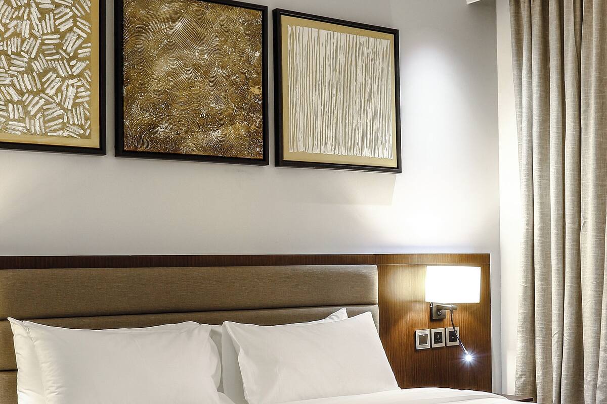 Ein Hotelzimmer mit einem großen Bett, einem hölzernen Kopfteil und drei gerahmten Kunstwerken an der Wand.