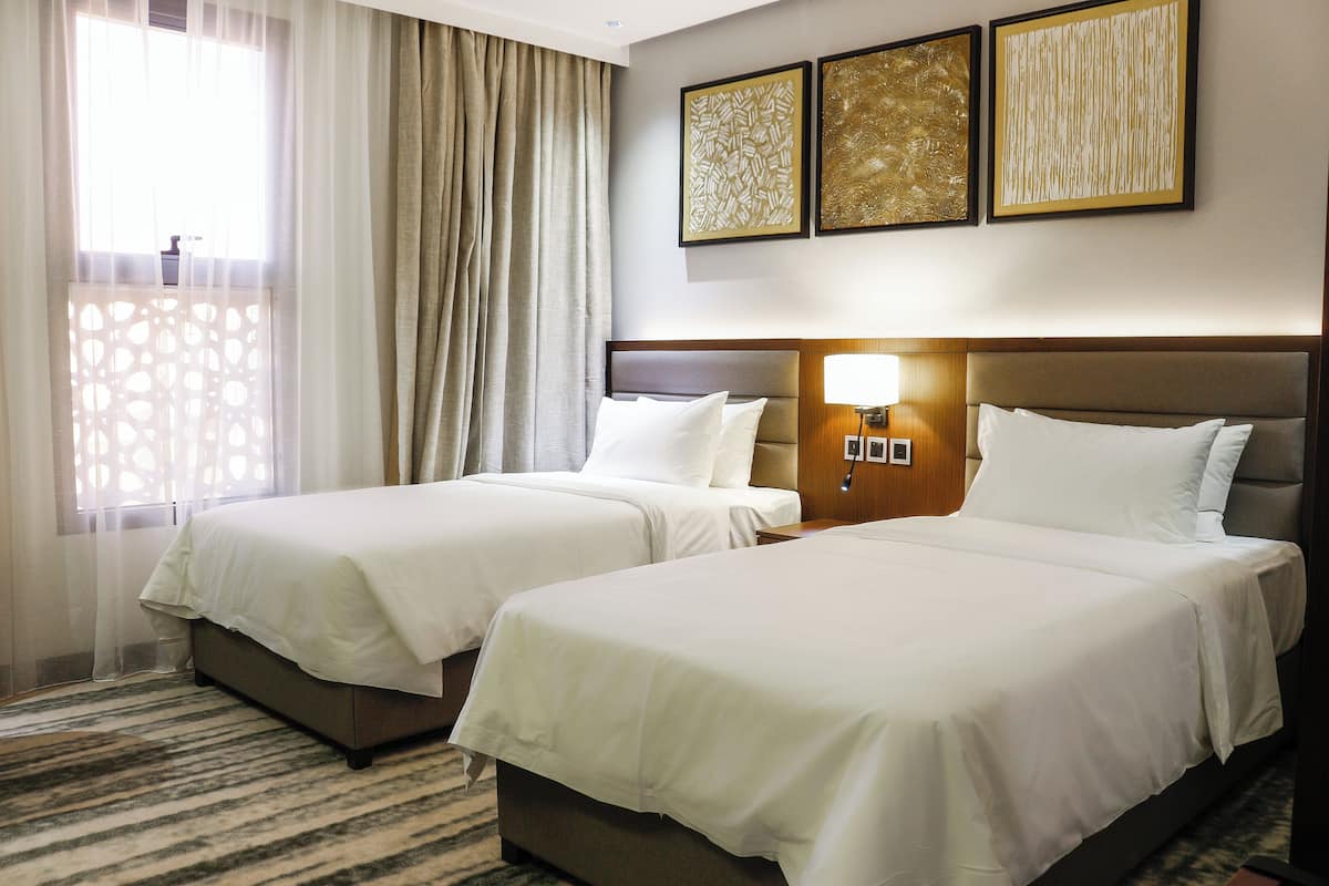 Ein Hotelzimmer mit zwei Betten, einem großen Fenster mit Vorhängen und drei gerahmten Kunstwerken an der Wand.