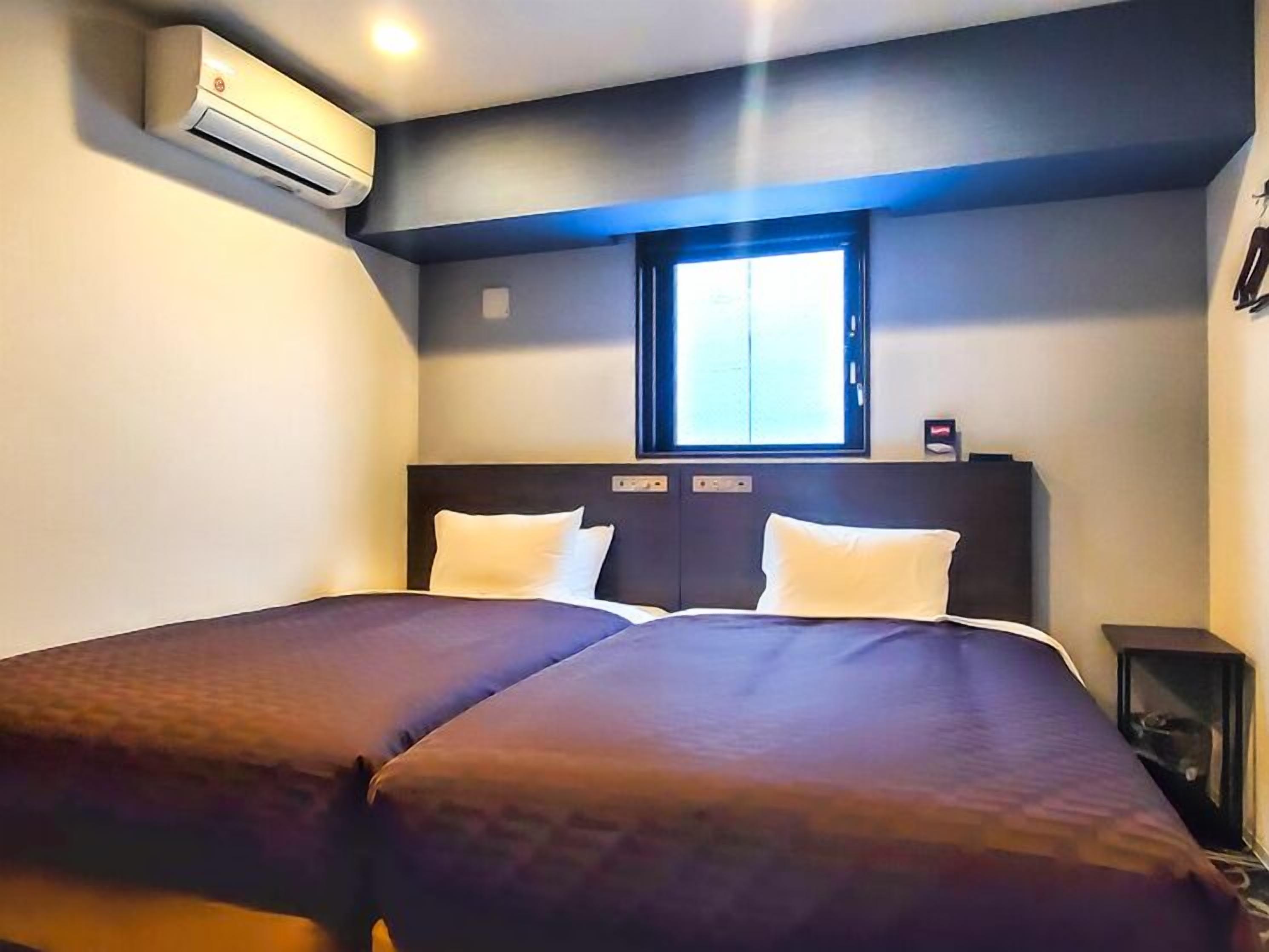 Une chambre d’hôtel avec deux lits, une fenêtre, un appareil de climatisation et une petite table.