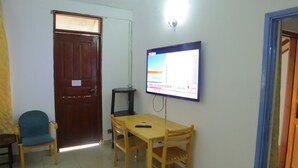 A small room with a wooden table, two chairs, a television mounted on the wall, and a door. - Kogelo Suites (Kisumu)