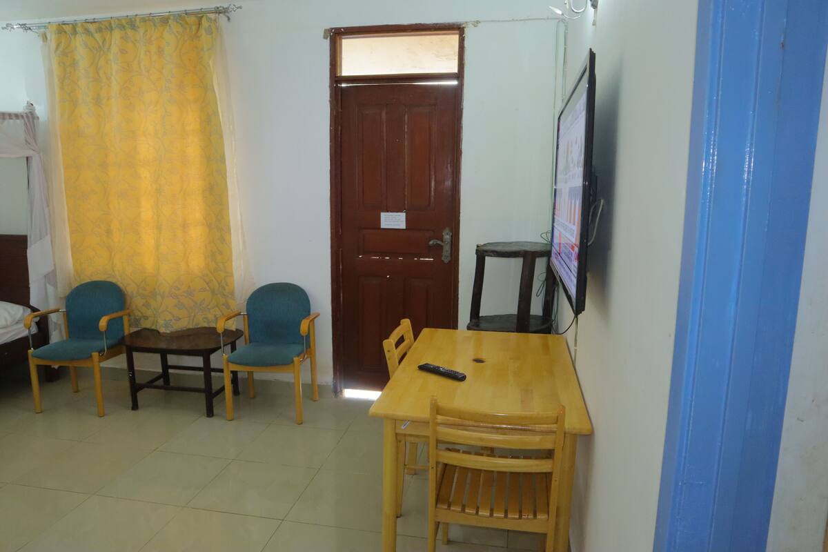 A room with a wooden table and chairs, a television mounted on the wall, and a door with a curtain.