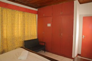 A room with a bed, a chair, and a wardrobe. - Kogelo Suites (Kisumu)