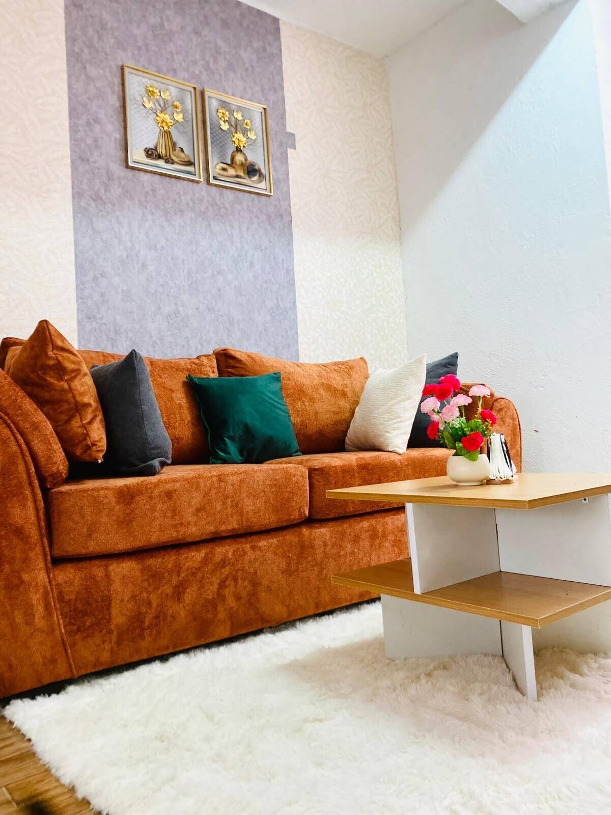 A living room with a brown sofa, a white furry rug, and a small wooden coffee table with a vase of flowers.