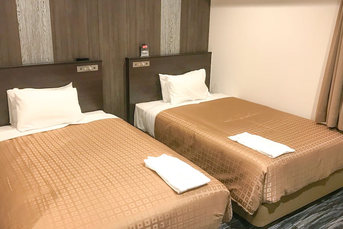 A hotel room with two beds, each with a patterned bedspread and white pillows.