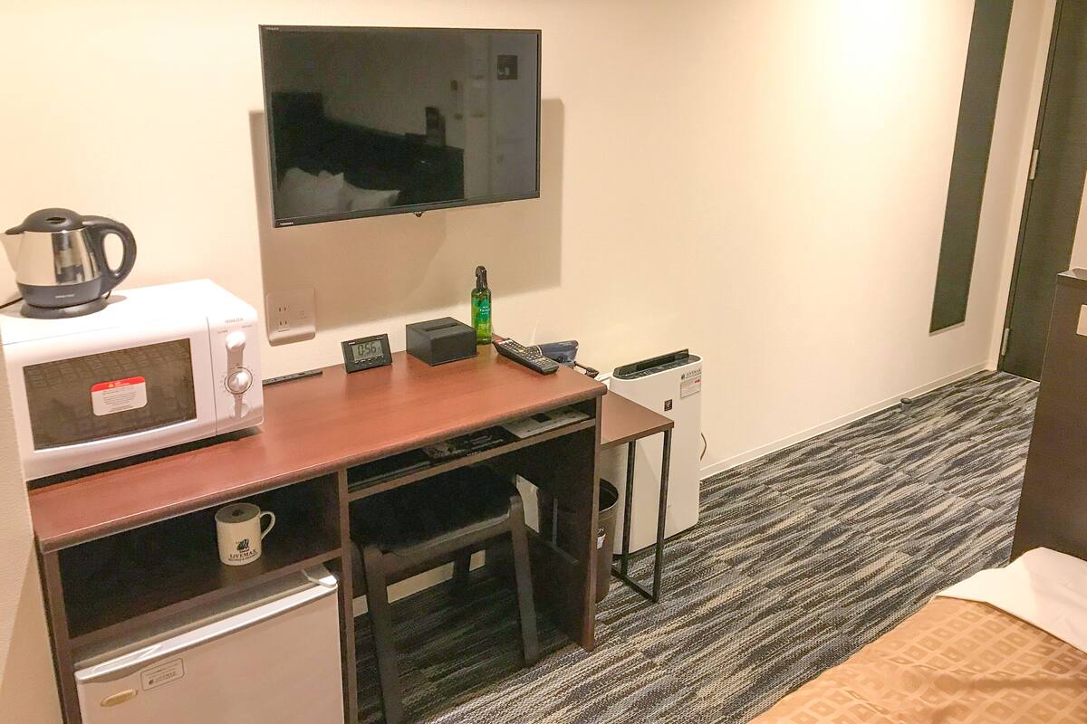 A hotel room with a kitchenette, a television mounted on the wall, a bed, and a carpeted floor.