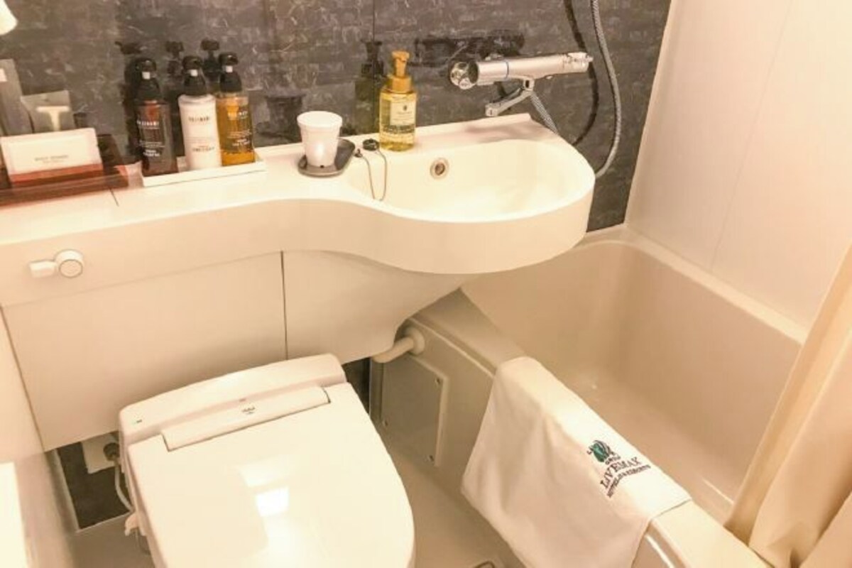 Un baño con lavamanos blanco, artículos de tocador, inodoro y toalla colgada en la pared.