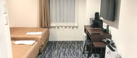 A small hotel room with two beds, a desk, a chair, a television, and a refrigerator.