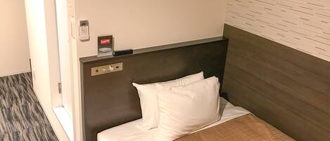A hotel room with a bed, a headboard, a control panel, and a wall-mounted air conditioning unit.