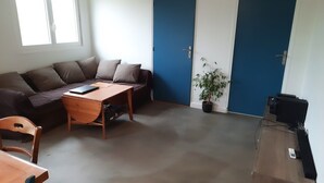 A living room with a sofa, a wooden table, a potted plant, and a door.