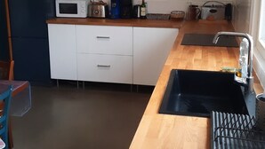 A kitchen with a wooden countertop, white cabinets, a microwave, a sink, and a framed picture on the wall.