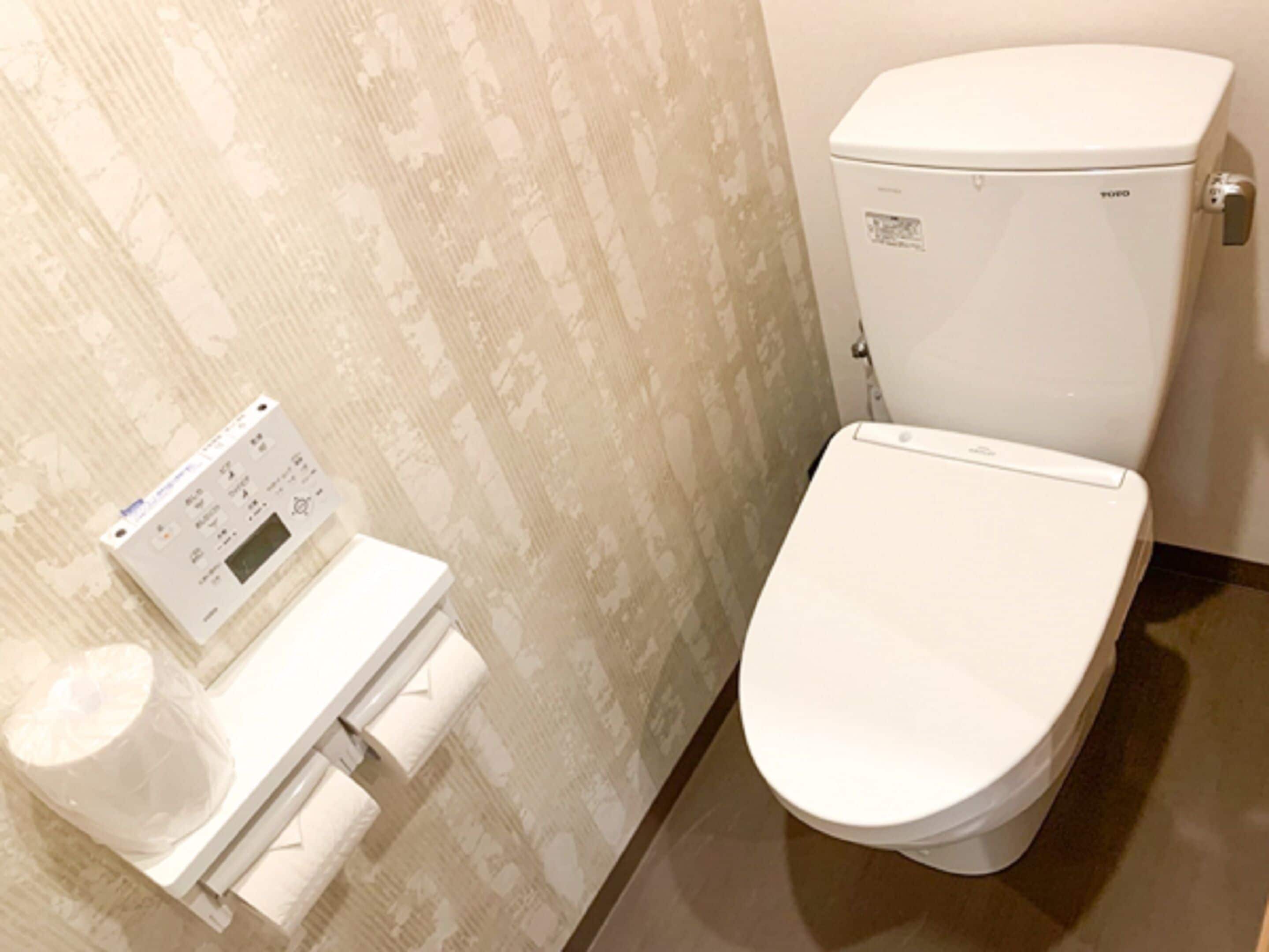 Un baño con un inodoro, un panel de control en la pared y un dispensador de papel higiénico.