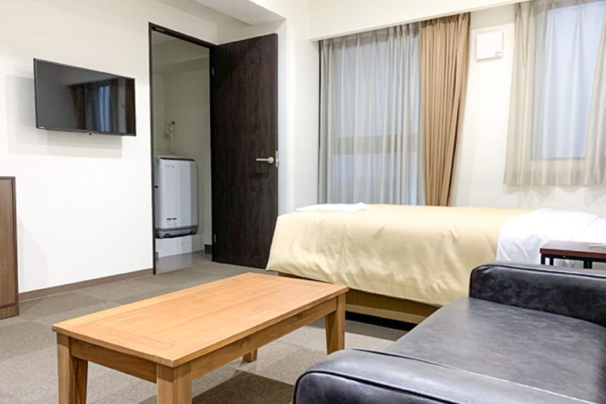 A hotel room with a bed, a sofa, a wooden table, a TV, and a heater.