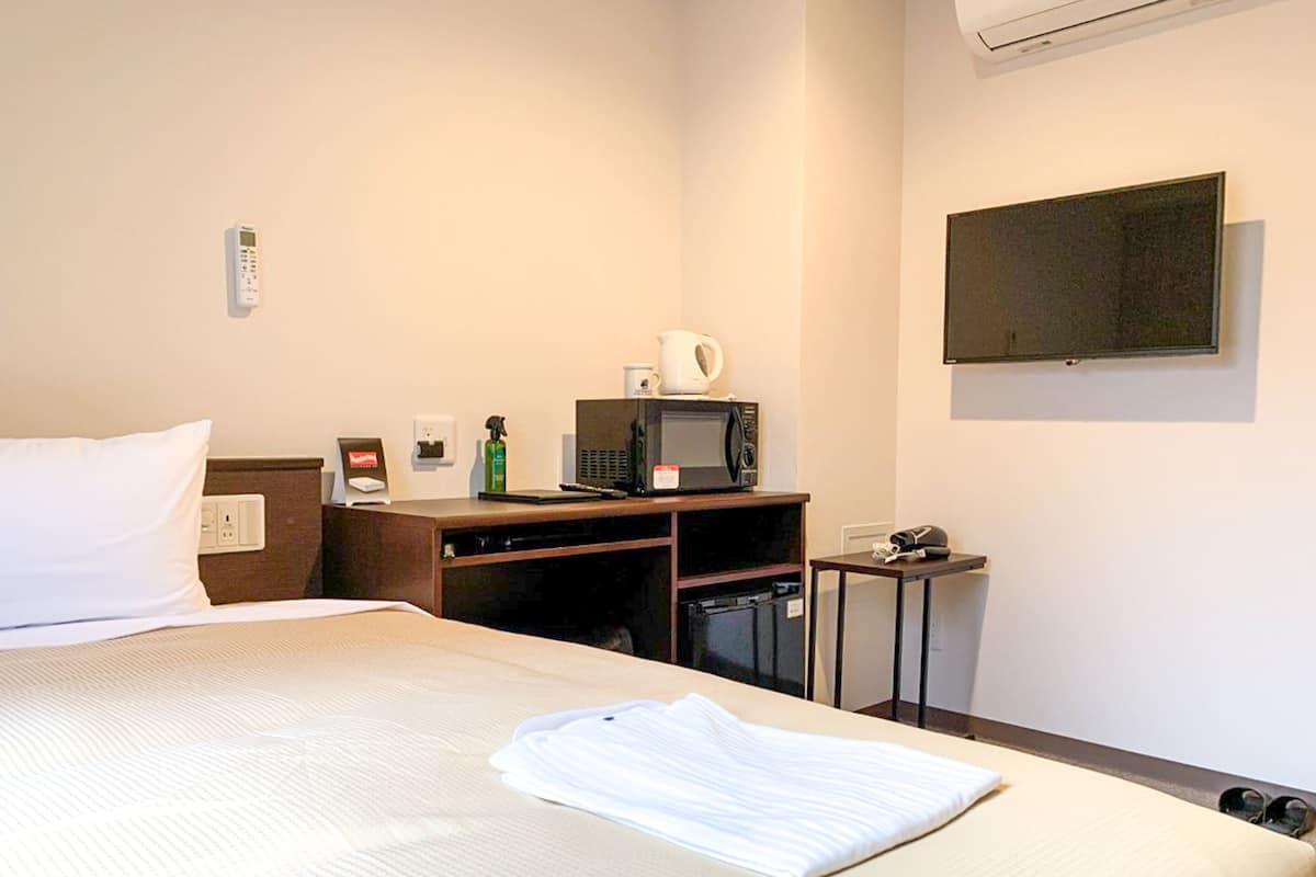 A hotel room with a bed, a desk with a microwave, a coffee maker, and a TV on the wall.