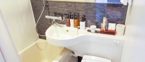 Une salle de bain avec un lavabo blanc, des toilettes et une douche. On trouve des articles de toilette sur le comptoir du lavabo.