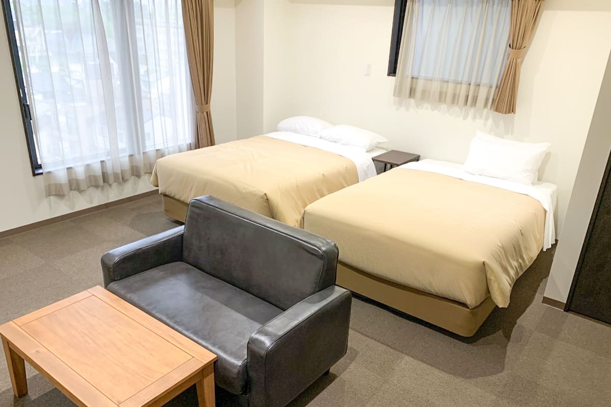 A hotel room with two beds, a sofa, and a small table.