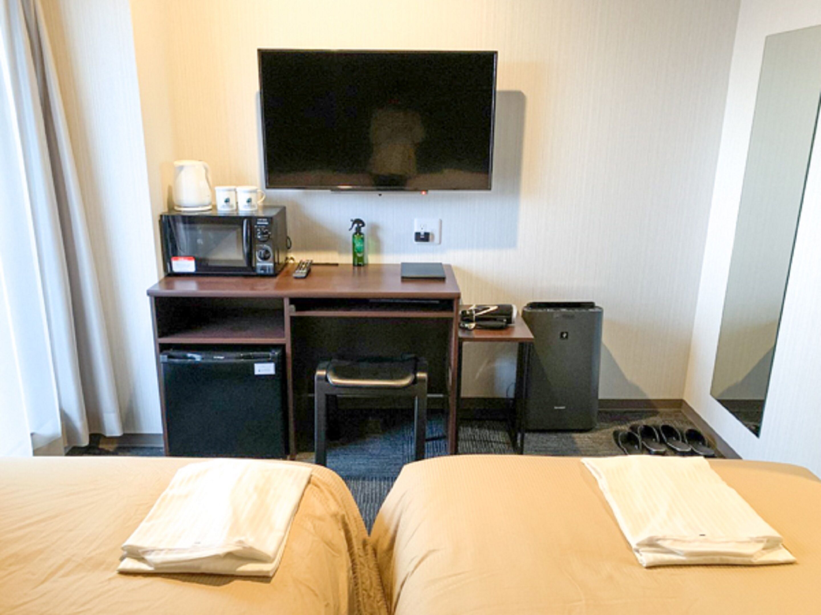 Une chambre d’hôtel avec deux lits, un bureau équipé d’un micro-ondes, une télévision, une poubelle et un petit réfrigérateur.