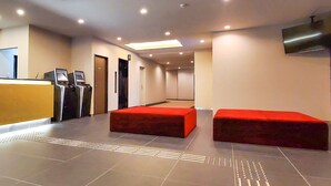 Eine moderne Lobby mit einer Rezeption, zwei roten Sitzbereichen und einem an der Wand befestigten Flachbildfernseher.