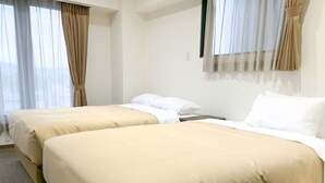Ein Hotelzimmer mit zwei Betten, beiger Bettwäsche, weißen Kissen und einem Fenster mit durchsichtigen Vorhängen.