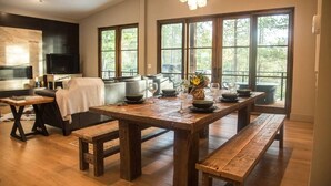 A modern kitchen with a large wooden table set for dining, a built-in oven, and large windows offering a view of the outdoors. - Gleneagles Golf Course Retreat with Hot Tub (Columbia Falls)
