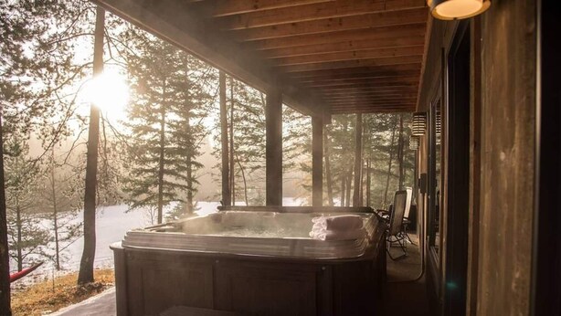 A hot tub on a wooden deck with a view of a forest and a lake. - Gleneagles Golf Course Retreat with Hot Tub (Columbia Falls)