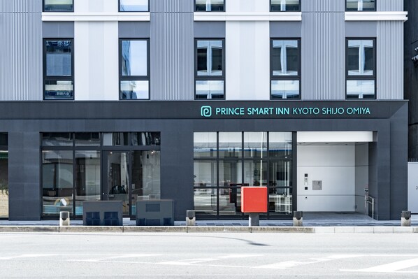 Ein moderner Hotel Eingang mit Glasfassade und einem Schild mit der Aufschrift "Prince Smart Inn Kyoto Shijo Omiya".