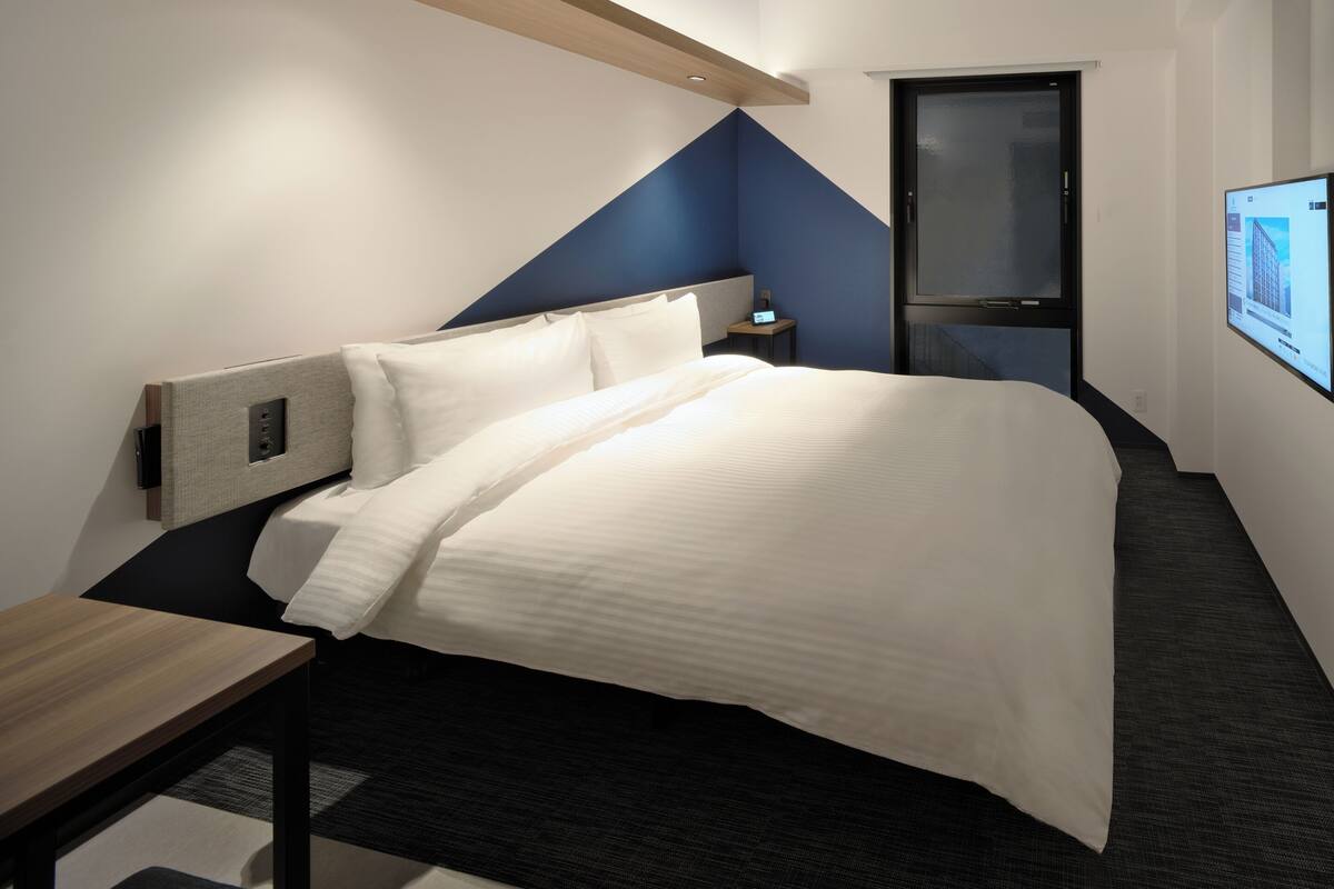A modern hotel room with a bed, bedside table, and a TV mounted on the wall.