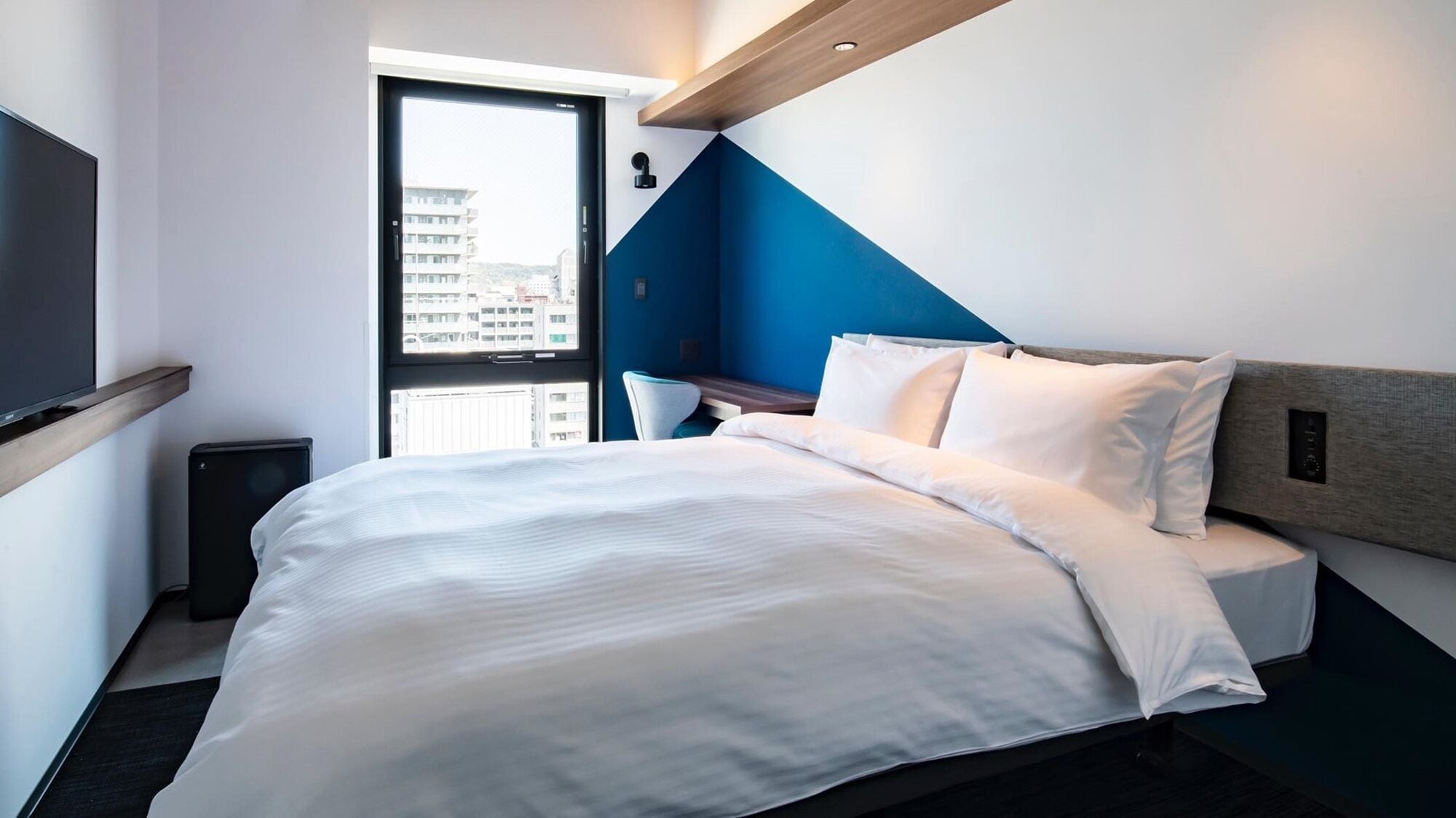 A modern hotel room with a bed, a desk, and a view through a door.