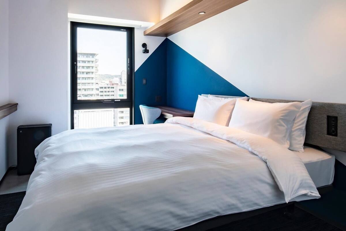 A modern hotel room with a bed, a desk, and a view through a door.