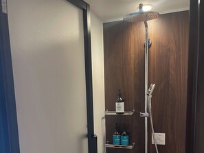 Eine Dusche mit Duschbrause, Wandarmatur und Ablage mit Flaschen.