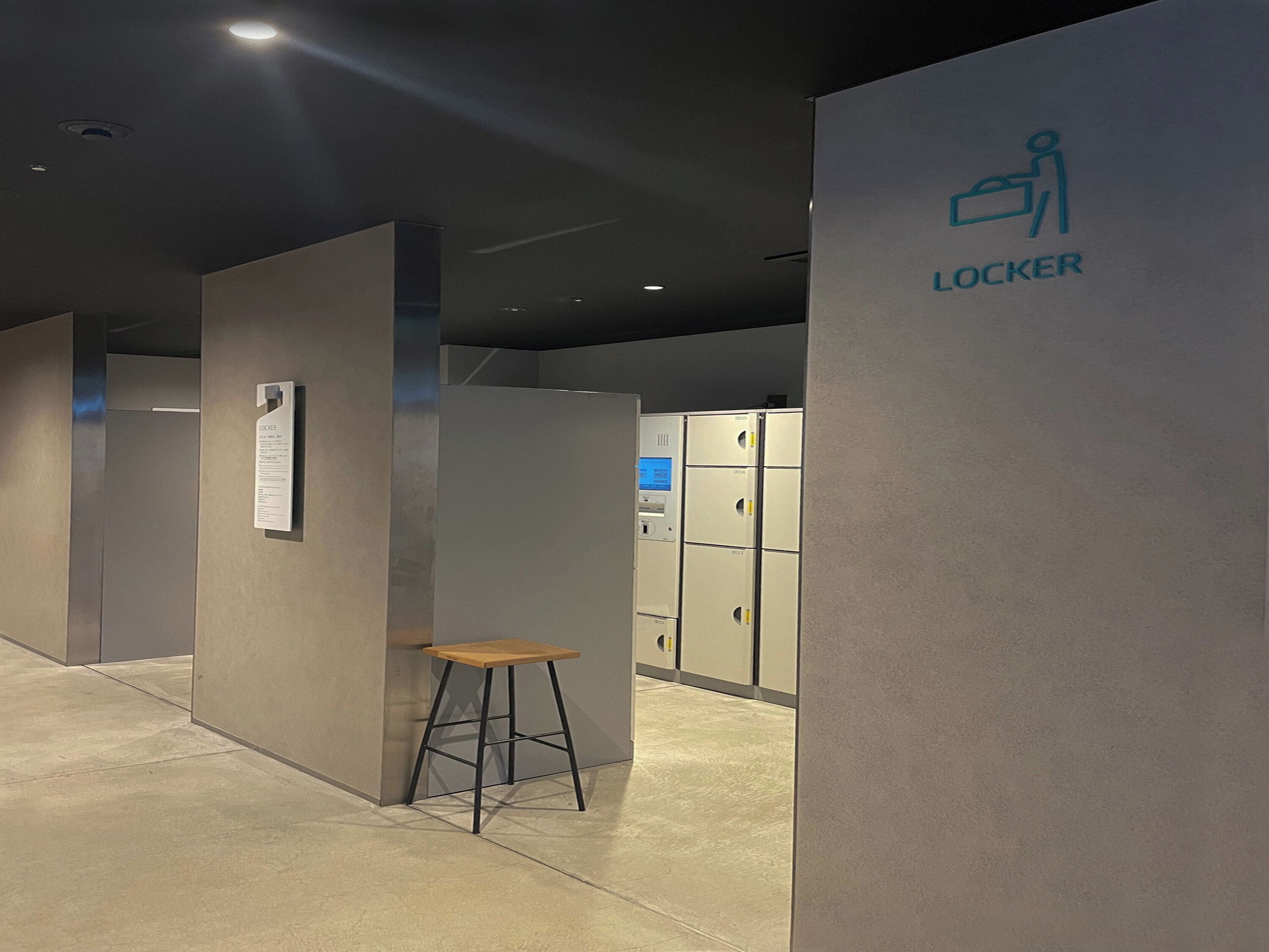 A modern hotel corridor with lockers, a wooden stool, and a sign indicating a locker room.