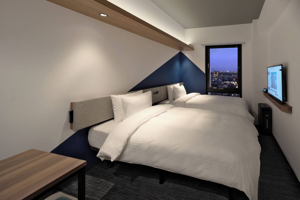 A modern hotel room with a large bed, a desk, and a city view through the window.