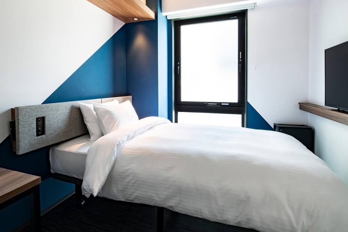 A modern hotel room with a bed, a desk, a TV, and a window.