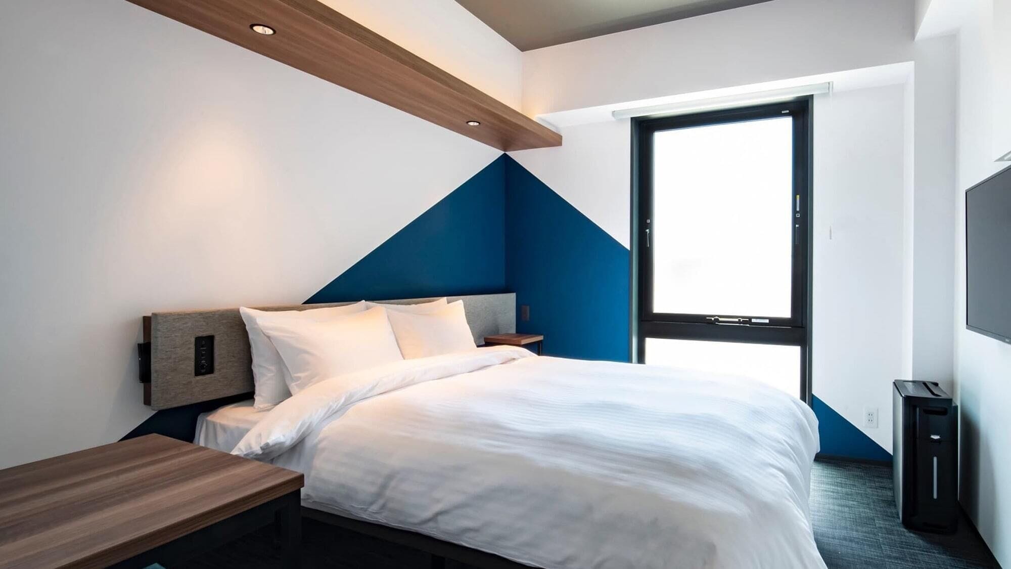 A modern hotel room with a bed, bedside table, and a large window.