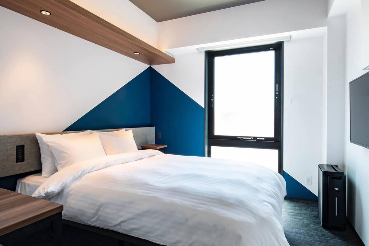 A modern hotel room with a bed, bedside table, and a large window.