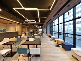 A modern cafe with tables and chairs, a counter, and large windows offering a view of the street.