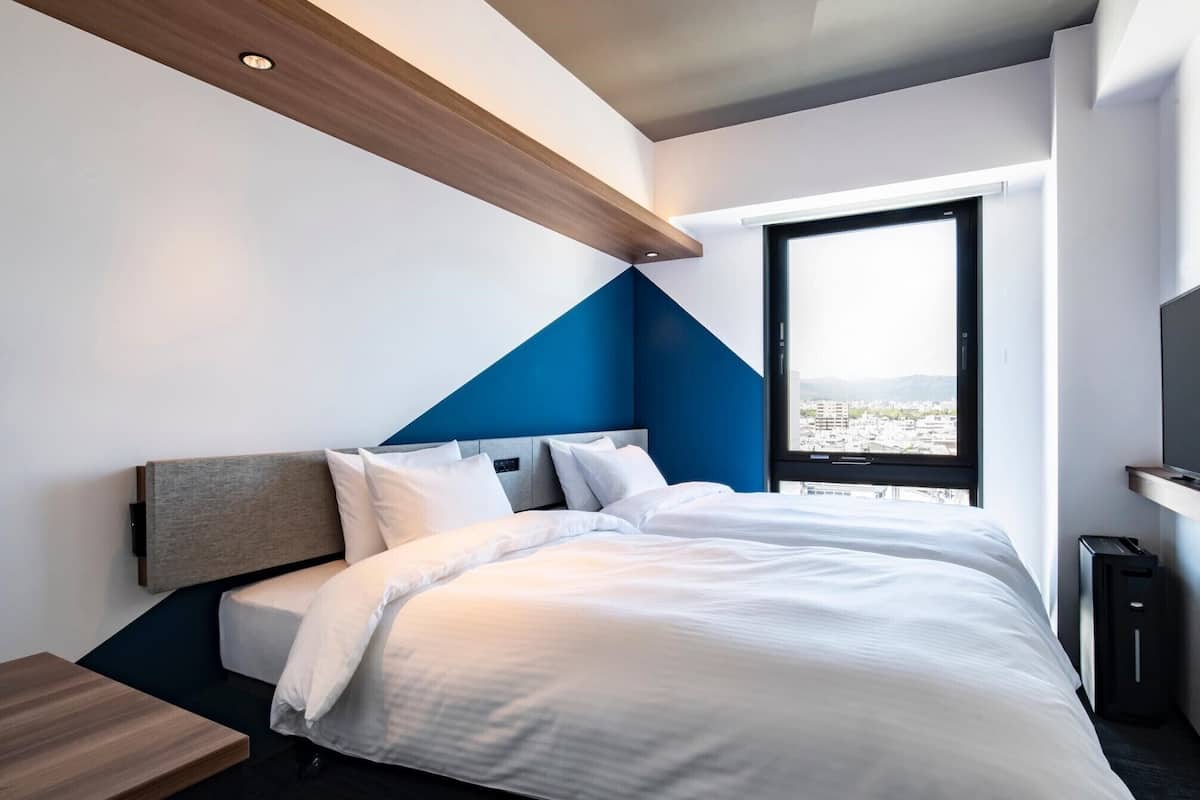 Ett modernt hotellrum med en säng, ett skrivbord, ett fönster med utsikt över staden och en TV.