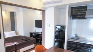 Une chambre d’hôtel compacte comprenant un lit, un bureau, une petite kitchenette et un coin repas avec deux chaises.
